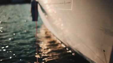 Altın güneş ışığı, sakin bir suda yüzen bir yatın kenarında parıldıyor.