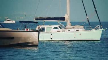 Parlak metalik bir yatın yan görüntüsü sakin mavi suda güneş ışığını yansıtıyor.