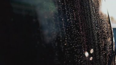 Arka plandaki bulanık bokeh ışıklarıyla hafifçe aydınlatılan cam pencerenin üzerindeki yağmur damlalarını kapat