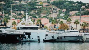 Yat üstü yatların panoramik manzarası yamaçtaki palmiye ağaçları ve pastel evler tarafından çerçevelenmiş bir marinada.