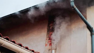 Eski bir tuğla bacadan solmuş bej bir duvara doğru yükselen yoğun beyaz bir duman.