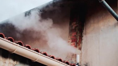 Eski bir tuğla bacadan solmuş bej bir duvara doğru yükselen yoğun beyaz bir duman.