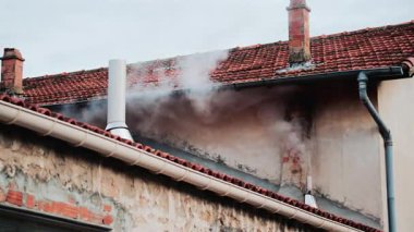 Eski bir tuğla bacadan solmuş bej bir duvara doğru yükselen yoğun beyaz bir duman.