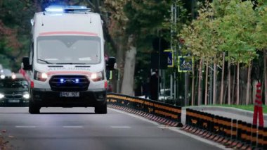 Chisinau, Moldova - 1 Ekim 2025: Alacakaranlıkta parlayan mavi ışıklarla bir şehir caddesinden geçen acil ambulans