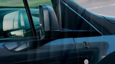 Yolun ve gökyüzünün ayna yansımalarını gösteren mavi bir minibüsün yan görüntüsü