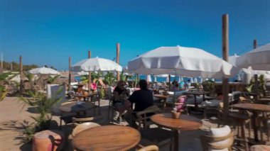 Cannes, Fransa - 3 Ekim 2025: Açık mavi gökyüzünün altında ahşap masalar, sandalyeler ve beyaz şemsiyeli sahil kafesi