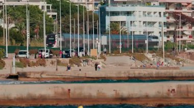 Cannes, Fransa - 8 Ekim 2025: İnsanlar yakınlarda yürüyüp dinlenirken modern bir tren sahilin kıyısından geçiyor.