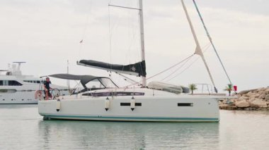 Cannes, Fransa - 12 Ekim 2025: Sakin bir günde bir marinadan ayrılırken beyaz yelkenliyi süren bir adam