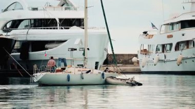 Küçük bir yelkenli, bir marinada büyük lüks yatların yanına yanaştı.