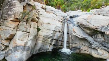 Baja California Sur, Meksika 'da çöl bitki örtüsü ve palmiyelerle çevrili kayalar arasında çağlayan küçük bir şelalenin hava aracı görüntüsü.