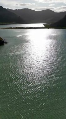 Baja California Sur 'daki kurak dağlarla çevrili, öğleden sonra güneşini yansıtan turkuaz deniz sularının insansız hava aracı görüntüsü. Dikey