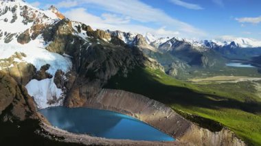 Dik kayalıklar ve karla kaplı zirveler arasında uzanan parlak turkuaz bir buzul gölü için insansız hava aracı görüntüsü