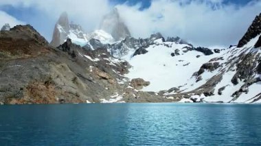 Fitz Roy 'un altındaki engebeli arazi ve kar tarlalarıyla çevrili turkuaz dağ gölünün insansız hava aracı görüntüsü.