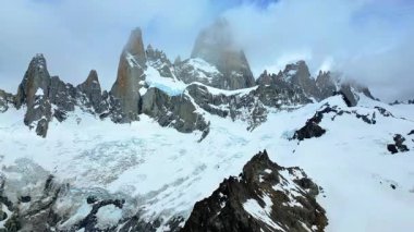 Fitz Roy 'un dramatik granit tepelerinin hava aracı görüntüsü kısmen buzullarla kaplı ve yamaçlara yayılmış bulutlarla kaplı.