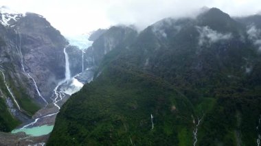 Sersemletici Ventisquero Colgante buzul şelalesinin hava aracı görüntüsü sarp kayalıklardan aşağı süzülüyor. Etrafı yemyeşil ormanlarla çevrili.