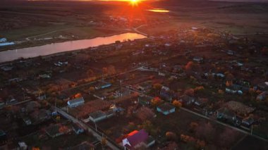 Gün batımında sakin bir nehrin yakınındaki Moldova köyünün insansız hava aracı görüntüsü