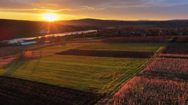 Hava aracı görüntüsü Moldova kırsalını gün batımında tarla desenleri ve uzakta parlayan bir nehirle gösteriyor.