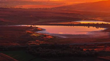 Moldova kırsalındaki günbatımının ılık altın ışığını yansıtan sakin bir göle ait hava aracı görüntüsü