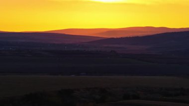 Moldova 'nın alacakaranlıktaki yuvarlanan tepelerini gösteren, parlak sarı turuncu gökyüzü ile kaplı, yumuşak ışıkla kaplı hava aracı görüntüsü.