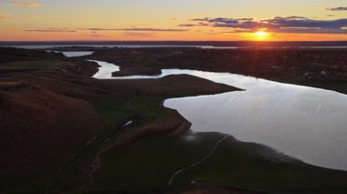 Dönen bir nehrin hava aracı görüntüsü Moldova 'nın kayan tepeleri ve uzak köyleri üzerindeki sıcak günbatımı ışığını yansıtıyor.