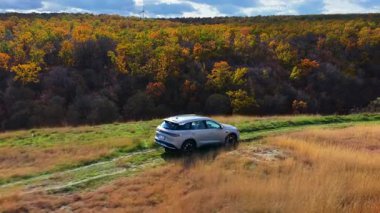Orhei, Moldova - 20 Ekim 2025: Çimenli tepelerde renkli sonbahar ormanlarıyla çevrili modern bir SUV 'un hava aracı görüntüsü