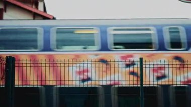 Bulanık yüksek hız treni, renkli grafiklerle metal bir çitin arkasından geçiyor, hareket, seyahat ve kentsel ulaşım altyapısını aktarıyor.