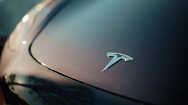 Cannes, Fransa - 1 Kasım 2025: Metalik mavi bir kaputun üzerindeki Tesla elektrikli araba logosuna yakın çekim, altın güneş ışığıyla aydınlatılmış, boyada hafif yansımalar var.