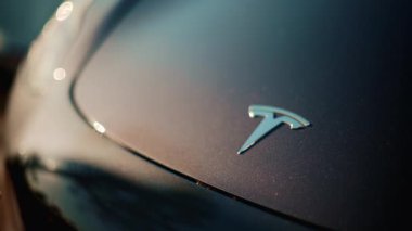 Cannes, Fransa - 1 Kasım 2025: Metalik mavi bir kaputun üzerindeki Tesla elektrikli araba logosuna yakın çekim, altın güneş ışığıyla aydınlatılmış, boyada hafif yansımalar var.