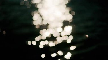 Işıldayan güneş ışığı, yumuşak deniz dalgalarına yansıyarak derin mavi bir su yüzeyinde parlak, ışıl ışıl bir bokeh oluşturur.