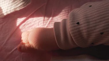 Bir bebeğin çıplak ayağını kapat. Yumuşak pembe bir battaniyenin üzerinde dinleniyor. Ilık pencere ışığıyla aydınlatılıyor.