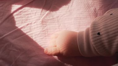Bir bebeğin çıplak ayağını kapat. Yumuşak pembe bir battaniyenin üzerinde dinleniyor. Ilık pencere ışığıyla aydınlatılıyor.