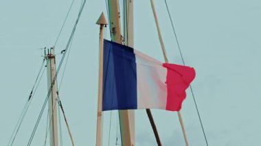 Fransız bayrağının yakınında, açık mavi gökyüzüne karşı bir gemi direğinde dalgalanan rüzgarda.