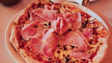 Üstünde ince dilimler halinde jambonlu taze pişmiş bir pizzanın resmi.