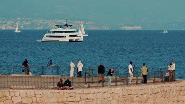 Antibes, Fransa - 10 Kasım 2025: Bir grup insan denize bakan bir taş rıhtım kenarında duruyor