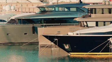Several modern luxury yachts lined up in a marina, reflecting warm sunlight on the calm water