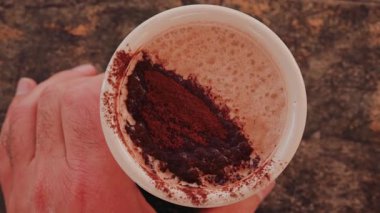 Kadının eli bir fincan sıcak çikolata tutuyor, üzerinde kakao tozu var.