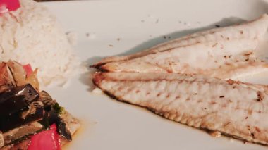 Izgara balık filetosu, beyaz pirinç, limon ve karışık sebzelerden oluşan dengeli bir restoran yemeği.