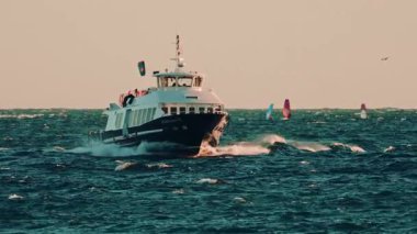 Cannes, Fransa - 18 Kasım 2025: Yolcu feribotu dalgalı sularda yüzüyor, kameraya doğru ilerliyor, rüzgar sörfçüleri uzaktan görülüyor.
