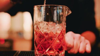 Bir barmenin bardağı buzla karıştırdığı yakın plan bir fotoğraf.