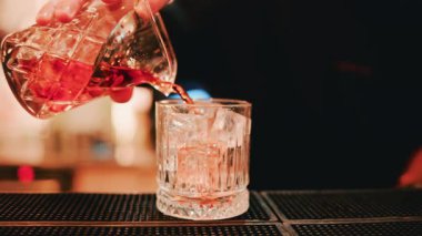 Yakın çekim, kristal karıştırıcı bardaktan buzla dolu bardağa akan yeni karışık bir kokteyl.