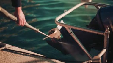 Yat limanının kenarındaki tekne pervanesini temizlemek için basınç makinası kullanan bir adama yaklaş.