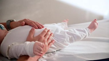 Bir bebeğin tıbbi muayene masasında sakince yatarken, elinde bir emzik tutarken bir yetişkinin nazikçe onları desteklemesi.