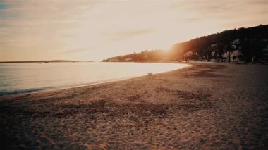 Gün batımında huzurlu bir sahil manzarası, kıyı şeridini aydınlatan yumuşak altın ışıkla.