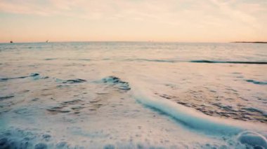 Gün batımında kumlu sahile yavaşça yuvarlanan küçük okyanus dalgalarını kapatın.
