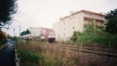 Golfe Juan, Fransa - 26 Kasım 2025: Hızlı hareket eden çift katlı bir tren, çevresindeki vahşi bitki örtüsüyle çevrili tren raylarından geçer