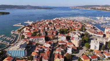 Biograd 'ın marina yakınlarındaki yerleşim bölgesinin hava aracı görüntüsü, arka planda görünen liman ve demirli tekneler ile kırmızı çatılı ev kümelerini gösteriyor. Biograd na Moru, Hırvatistan