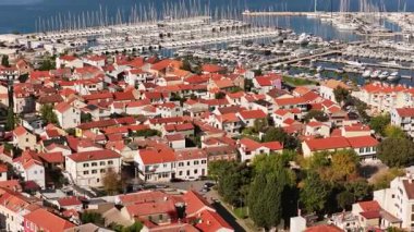 Biograd 'ın marina yakınlarındaki yerleşim bölgesinin hava aracı görüntüsü, arka planda görünen liman ve demirli tekneler ile kırmızı çatılı ev kümelerini gösteriyor. Biograd na Moru, Hırvatistan