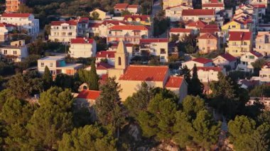 Hırvatistan 'ın Tribunj kentinde gün batımında çan kulesi olan küçük taştan bir kilisenin insansız hava aracı görüntüsü