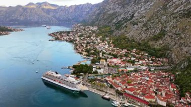 Eski kasabanın, limanın ve körfezdeki bir yolcu gemisinin hava aracı görüntüsü, dik dağlar tarafından çerçevelenmiş ve Kotor körfezindeki temiz sabah ışığı