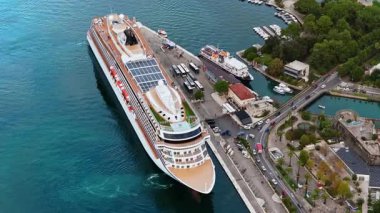 Kotor limanına yanaşan büyük bir yolcu gemisinin hava aracı görüntüsü, otobüsler, marina ve liman altyapısı görünür.